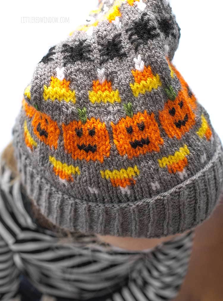 closerup of jack o lantern candy corn and spider details on Halloween stocking cap knitting pattern on a gray background