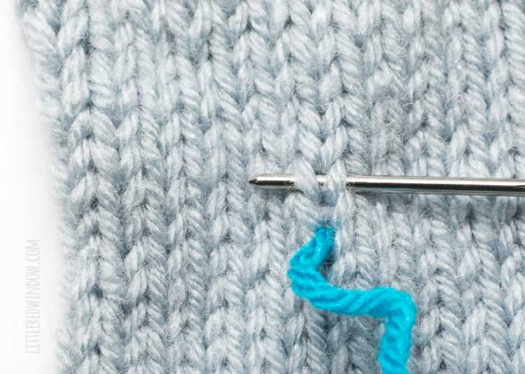 showing where to insert the yarn needle for the second step of duplicate stitch in knitting