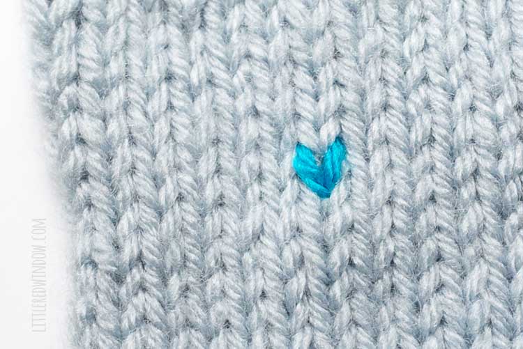 one finished electric blue duplicate stitch on a field of light blue stockinette stitch knitting