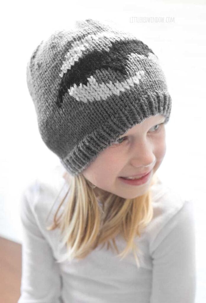 view from slightly above of little girl in white shirt wearing gray knit hat with white crescent moon and black bat looking off in the distance to the right and smiling