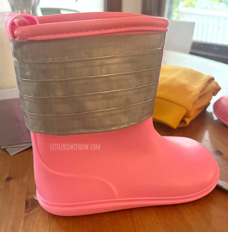 a pink rainboot with lines of silver duct tape around the top sitting on a wood table