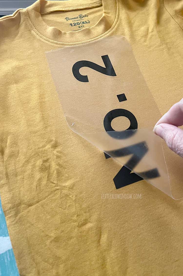 a hand peeling off the clear backing from the black heat transfer vinyl No 2 on the yellow pencil costume shirt