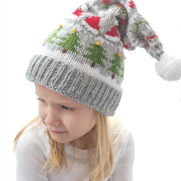 blond girl in white long sleeved shirt wearing a gray knit stocking cap decorated with patterns of Christmas trees Santa hats holly berries and candy cane stripe and a white pom pom on top looking down and off to her left