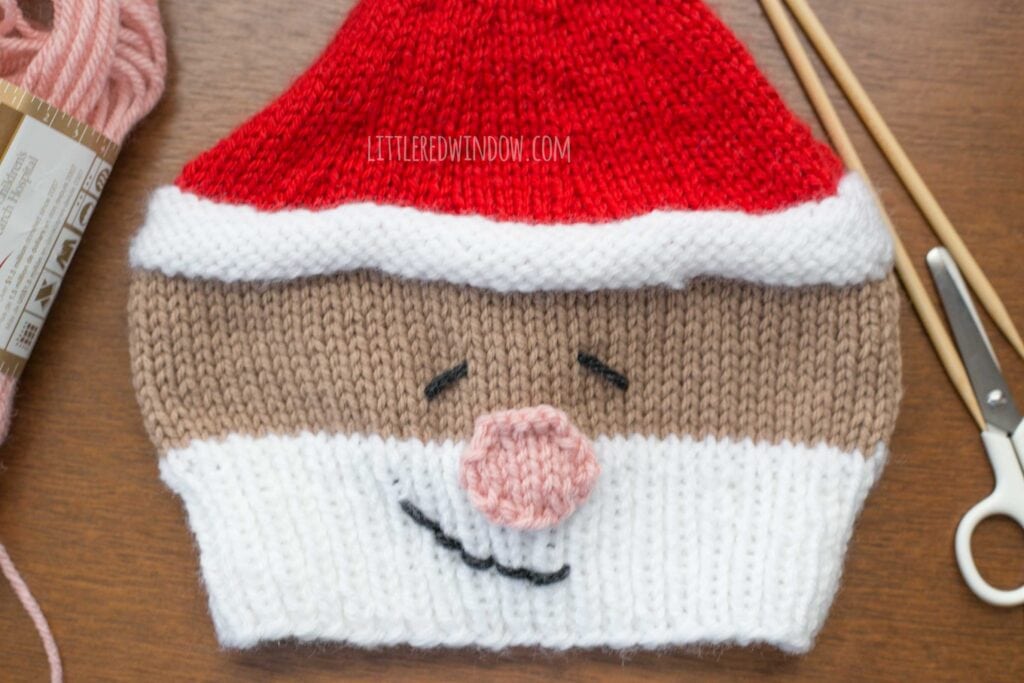 closeup of a finished smiling santa hat on a tabletop showing how to embroider the eyes and smile on the front of the hat