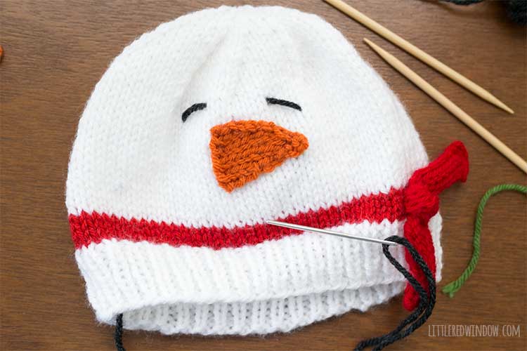 snowman hat with black yarn used to stitch two eyes above the carrot nose