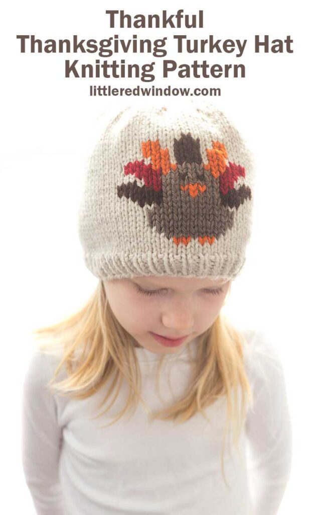 girl in white shirt wearing a tan knit hat with a Thanksgiving Turkey knit on the front 