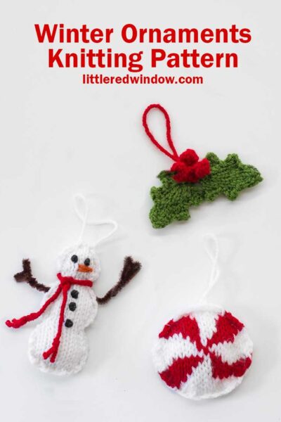 Three knit Christmas tree ornaments in the shape of a snowman a round red and white peppermint candy and a pair of holly leaves with red berries on a white background