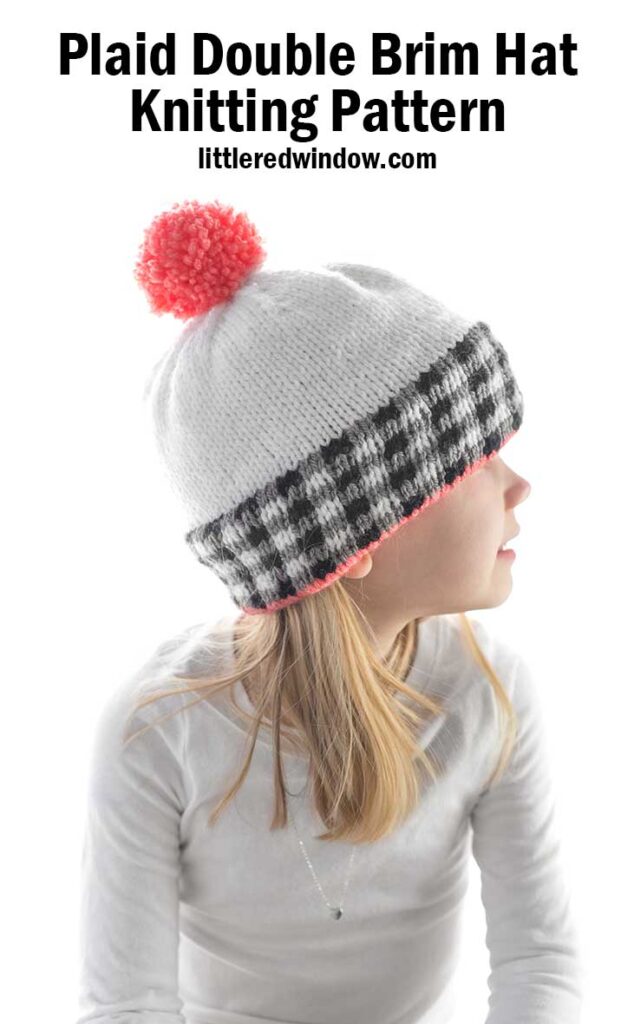 girl in white shirt wearing a white knit hat the black and white plaid brim and pink pom pom on top looking off to the right