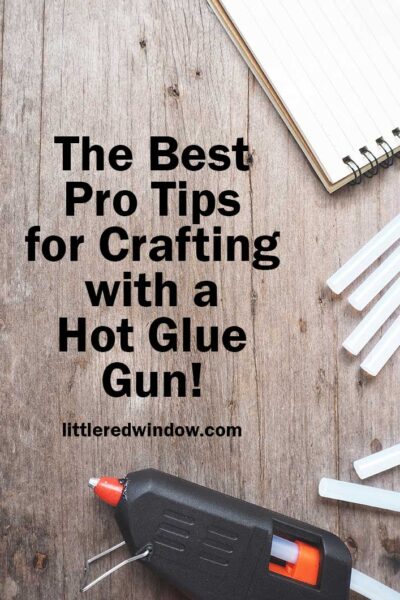 A black hot glue gun with hot glue sticks and a white notepad on a gray wood background
