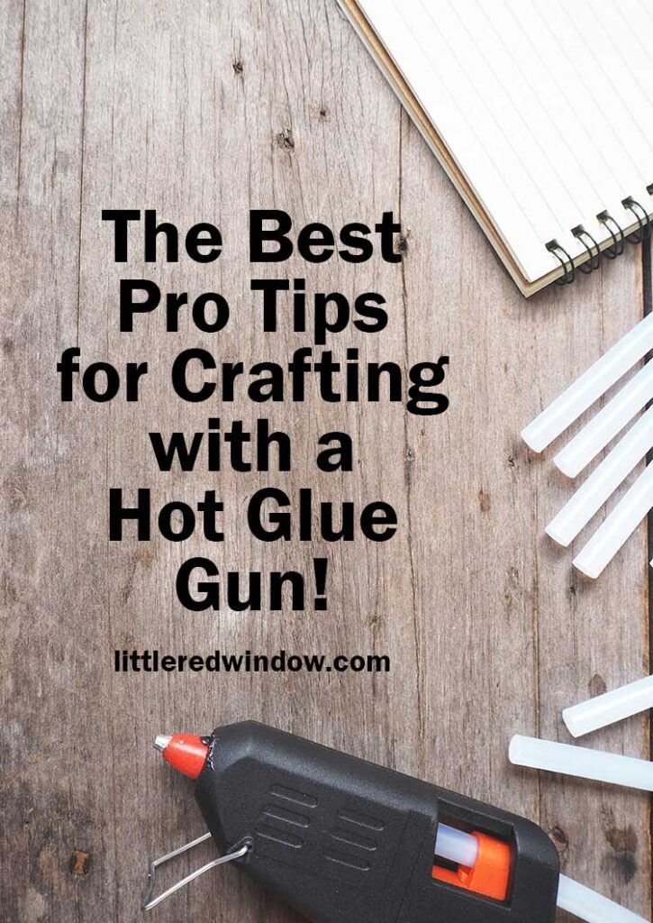 A black hot glue gun with hot glue sticks and a white notepad on a gray wood background