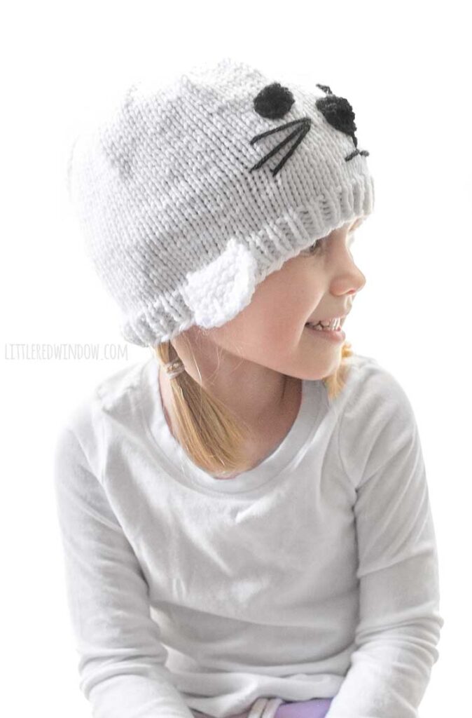 girl wearing white seal knit hat and looking off to the right