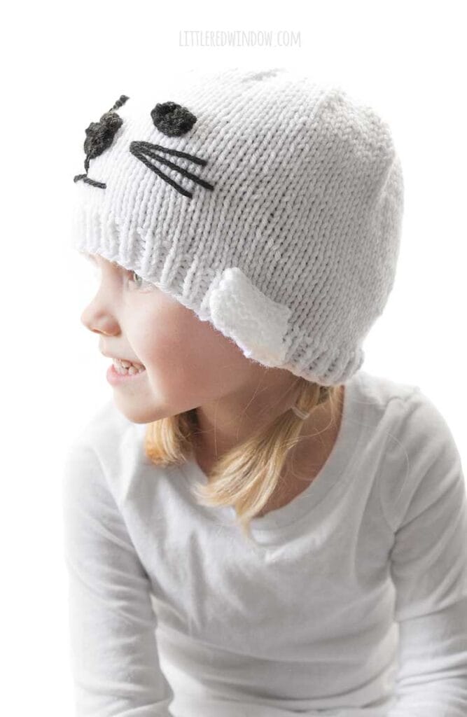 girl wearing white seal knit hat and looking off to the left