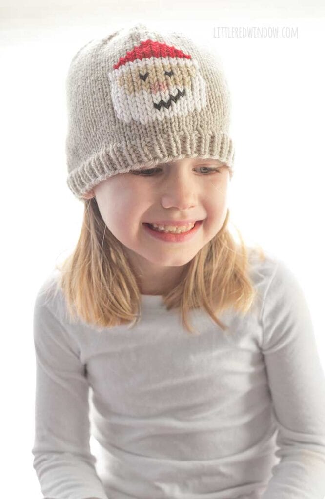 Laughing girl wearing tan knit hat with Santa face on the front