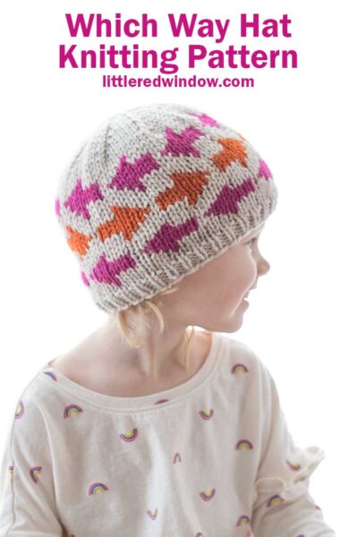 little girl wearing tan knit hat with pink and orange arrow shapes on it looking off to the right