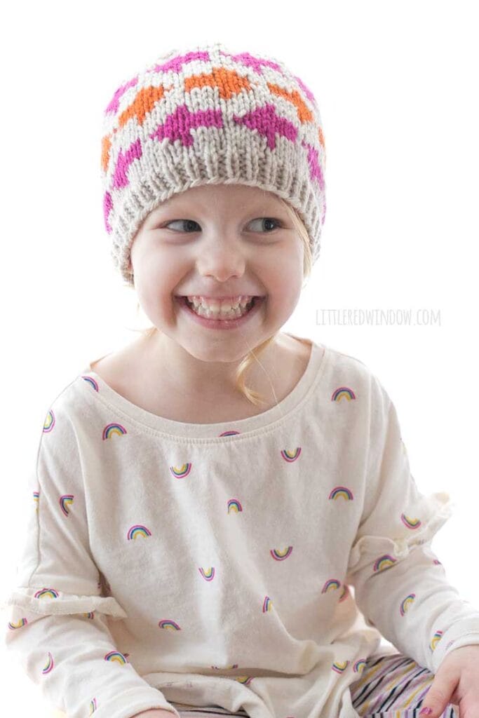 smiling girl wearing which way arrow hat with pink and orange arrow shapes on it