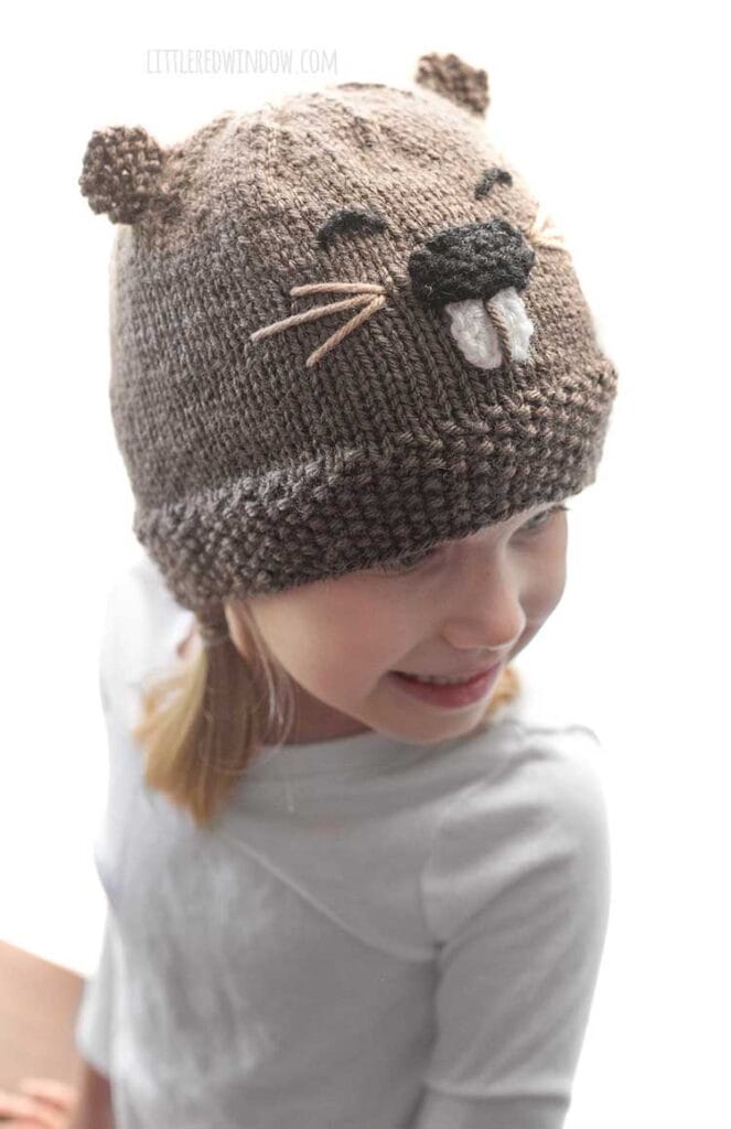 girl wearing brown knit beaver face hat looking back over her left shoulder