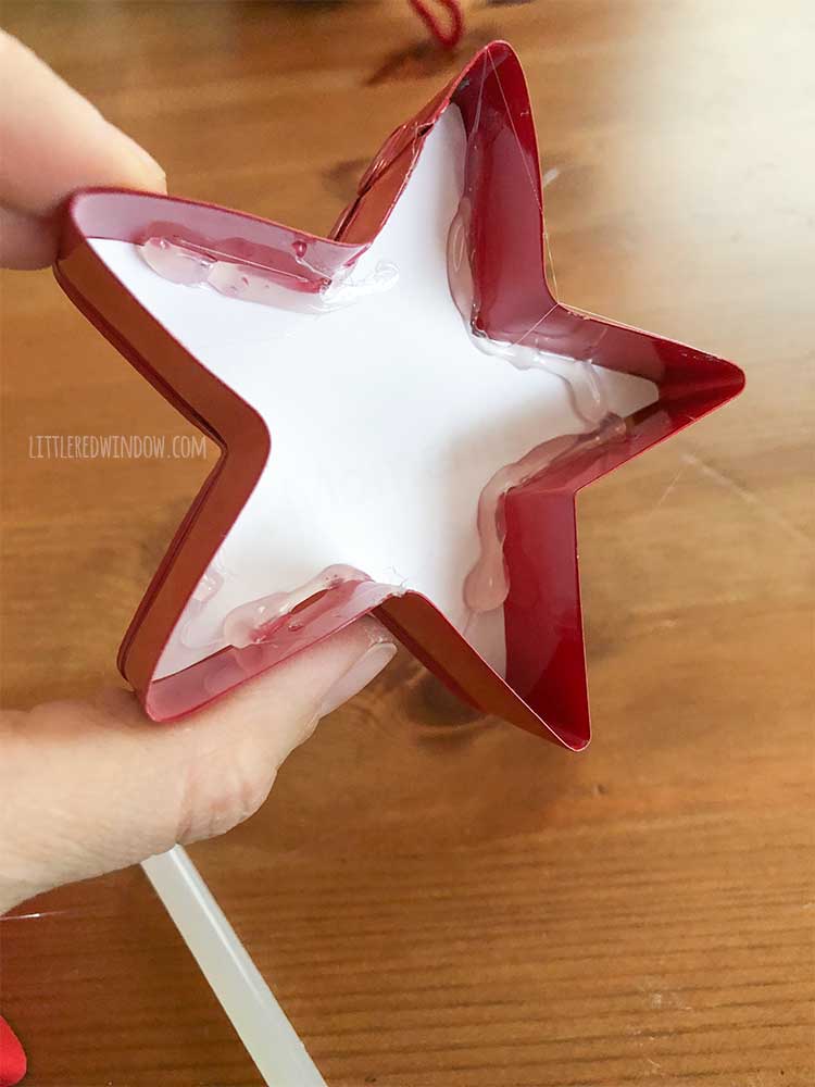 hand holding red star shaped cookie cutter with the back of a white photo hot glued inside of it