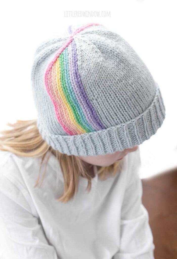 view from slightly above of child wearing rainbow twirl hat in front of a white background