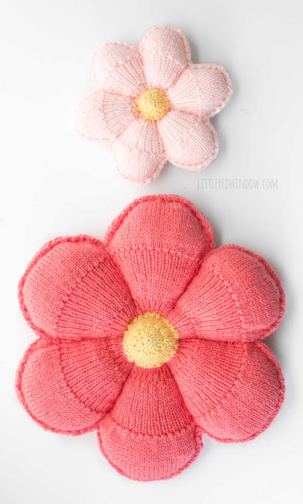 small light pink knit flower pillow above a dark pink large knit flower pillow on a flat white background