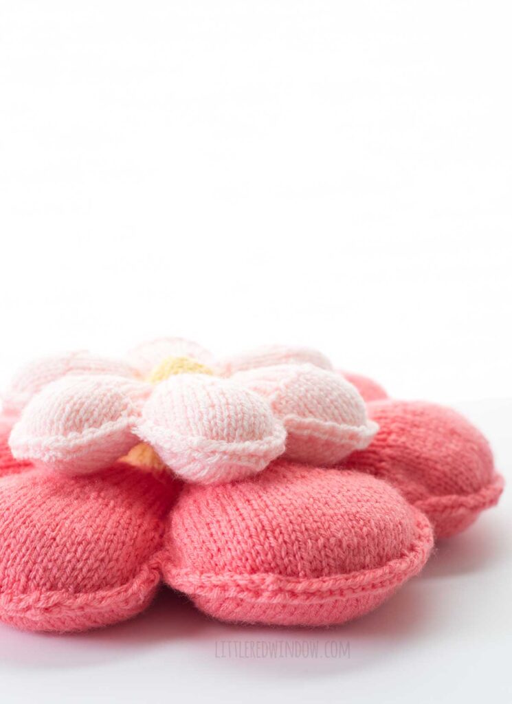 side view showing thickness of large and small pink knit flower pillows stacked on top of each other in front of a white background