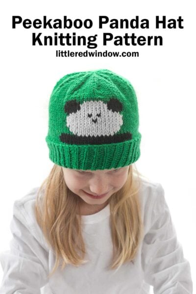 Blond girl in white shirt wearing a kelly green knit hat with folded ribbed brim that has a panda face peeking out over the brim while she is smiling and looking down