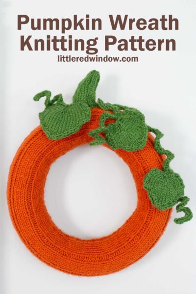A knitted pumpkin wreath adorned with green leaves and vines, resembling a festive pumpkin. The text 