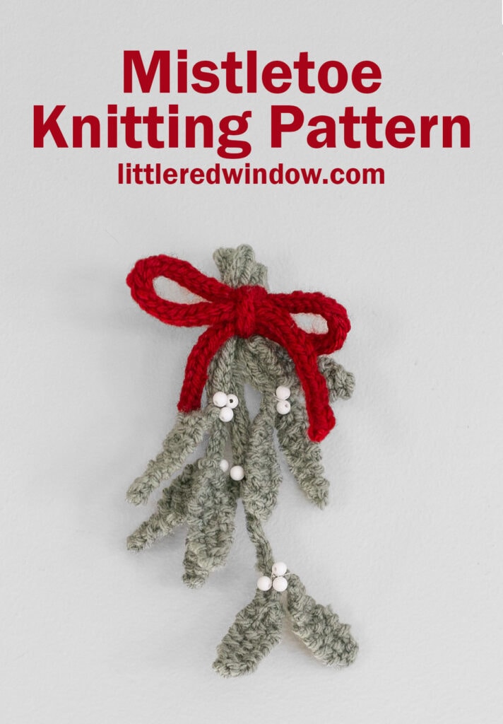 Knitted mistletoe with green leaves, white berries, and a red bow on a light background. Text above reads: