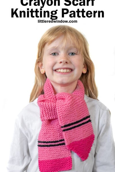 Smiling child wearing a pink and magenta crayon scarf with black stripes over a white shirt. Text above reads,