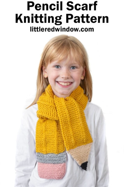Smiling young girl wearing a scarf designed to look like a yellow pencil, with pink, gray, beige, and black ends. Text above reads